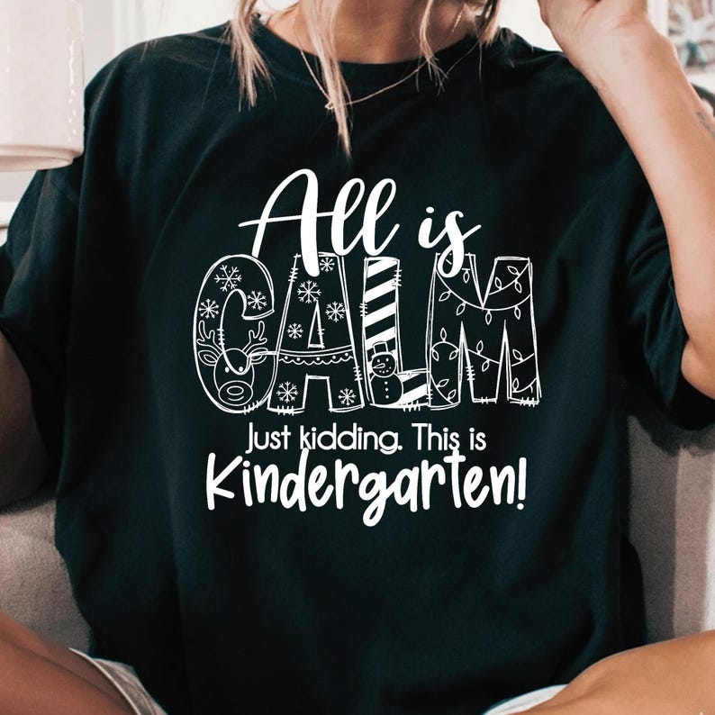 May include: Black t-shirt with the words "All is CALM" in white, with snowflake and holiday-themed designs incorporated into the letters. Below, the text reads "Just kidding. This is Kindergarten!"