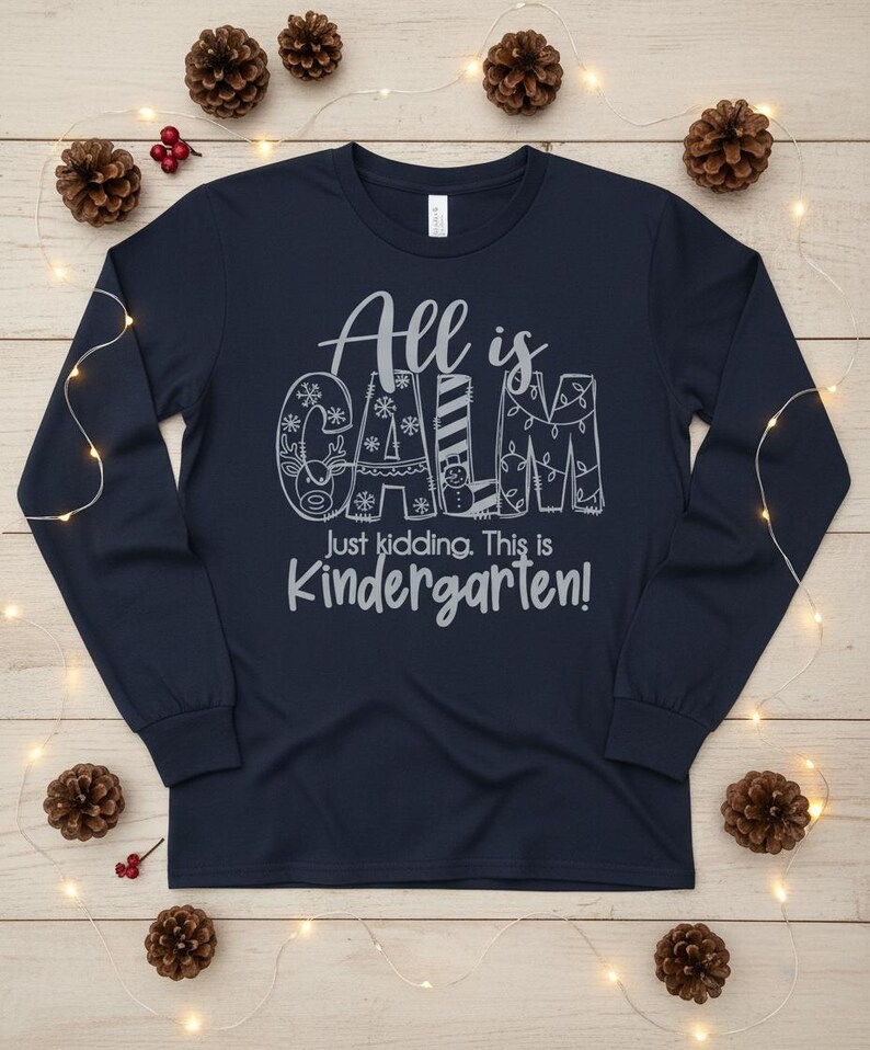 May include: Navy blue long-sleeve shirt with the text "All is CALM, Just kidding. This is Kindergarten!" in a whimsical font. The word "CALM" is decorated with snowflakes, a reindeer, a snowman, and Christmas lights.