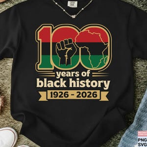 Könnte beinhalten: Schwarzes T-Shirt mit einer Grafik, die 100 Jahre schwarzer Geschichte feiert. Das Design zeigt die Zahl 100 in Rot, Grün und Schwarz, eine geballte Faust und den afrikanischen Kontinent. Der Text lautet "years of black history 1926-2026."