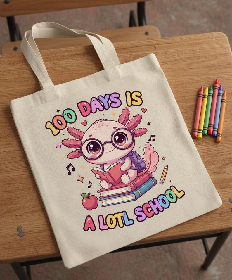 May include: A cream-colored tote bag with the text "100 DAYS IS A LOTL SCHOOL" and a cartoon axolotl wearing glasses and a backpack, reading a book. Colorful crayons are to the right.