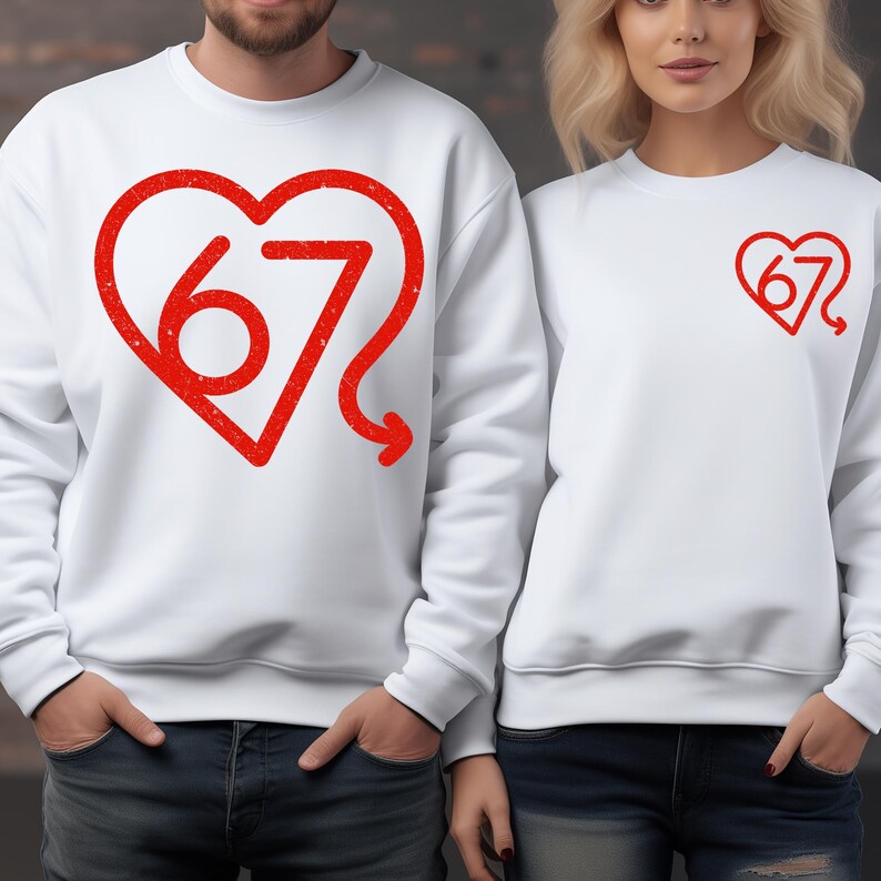 Puede incluir: Dos sudaderas blancas con dise&ntilde;os de coraz&oacute;n rojos. Una sudadera presenta un coraz&oacute;n grande con el n&uacute;mero "67" en su interior, y la otra tiene un coraz&oacute;n m&aacute;s peque&ntilde;o con el mismo n&uacute;mero. Las sudaderas son usadas por dos personas.