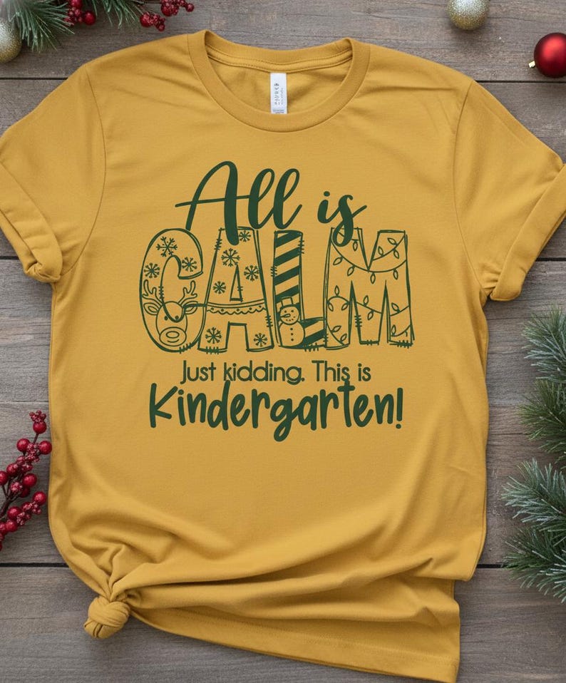 May include: Mustard yellow t-shirt with the text "All is CALM" in dark green, with the letters decorated with snowflakes, a reindeer, and Christmas lights. Below, it reads "Just kidding. This is Kindergarten!"
