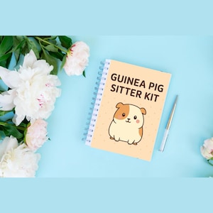 Op de afbeelding: Een spiraalgebonden notitieboek met de tekst "GUINEA PIG SITTER KIT" en een cartoonillustratie van een cavia. Een zilveren pen ligt naast het notitieboek op een lichtblauwe ondergrond, met witte en roze bloemen op de achtergrond.