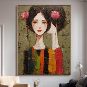 May include: Large framed abstract painting of two female figures with dark hair and pink accents. They wear colourful striped clothing against an olive green textured background. The artwork is displayed in a room with neutral tones and a wooden floor.