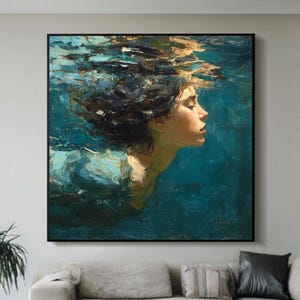 Op de afbeelding: Groot ingelijst kunstwerk met een abstract schilderij van een persoon die onder water zwemt. Het kunstwerk heeft een teal- en goudkleurig kleurenpalet, met een donkere lijst. Het schilderij wordt tentoongesteld boven een lichtgekleurde bank in een moderne woonkamer.