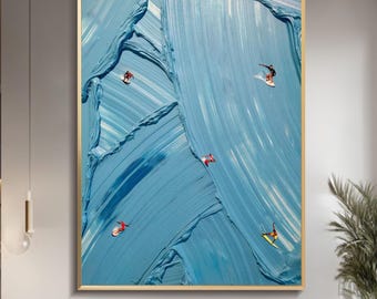 Op de afbeelding: Groot abstract schilderij met gouden lijst. Het kunstwerk heeft een getextureerde, blauwe achtergrond met verschillende kleine surfende figuren. Het schilderij wordt tentoongesteld in een moderne woonkamer met een bank, stoelen en een salontafel.