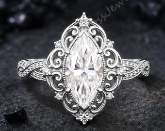 May include: A silver-toned ring featuring a central marquise-cut clear gemstone surrounded by an intricate filigree metal setting. The band displays a twisted design and is accented with small, round, clear stones along the shoulders.