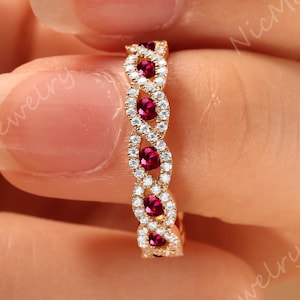 May include: A gold band ring featuring a twisted rope design set with alternating round red rubies and small clear white diamonds. The metal has a polished finish, and the stones are arranged in a repeating pattern along the center of the band.