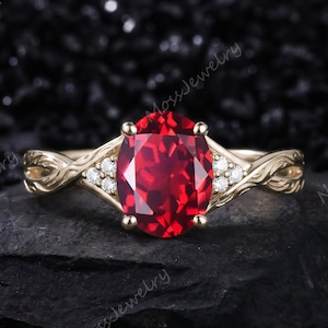Puede incluir: Un anillo de oro con una gran piedra preciosa de color rojo intenso de corte ovalado como pieza central, flanqueada por tres pequeñas piedras blancas redondas a cada lado. La banda muestra una textura intrincada de enredadera.