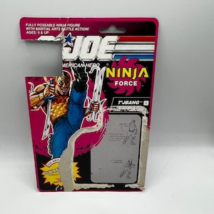 May include: A vintage action figure package for a Ninja Force T'Jbang figure. The packaging is pink and black with the words "Ninja Force" and "American Hero" printed on it. The figure is fully poseable with martial arts battle action.