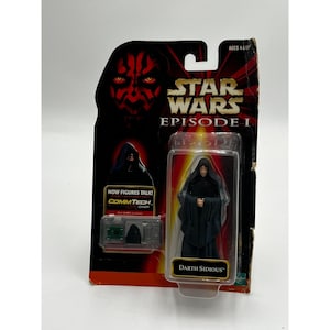 Könnte beinhalten: Star Wars Episode I Actionfigur von Darth Sidious, verpackt in einer transparenten Kunststoffhülle. Die Verpackung ist rot und schwarz, mit dem Star Wars-Logo und dem Text "NOW FIGURES TALK! COMMTECH CHIP". Die Figur trägt eine schwarze Robe.
