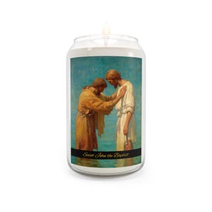 Puede incluir: Una vela blanca con una imagen pintada de San Juan Bautista bautizando a Jesús. La imagen presenta dos figuras con túnicas fluidas sobre un fondo azul. El texto "Saint John the Baptist" está impreso en una pancarta negra en la parte inferior.