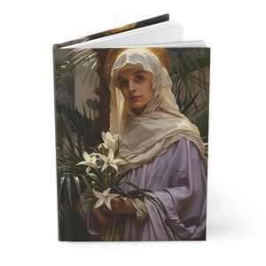 May include: Hardcover journal featuring a classical painting of a woman with a halo, holding white lilies. The artwork is set against a backdrop of lush green foliage. The journal's cover has a matte finish.
