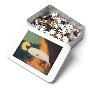 May include: A white tin box containing a colourful jigsaw puzzle. The puzzle shows a man in a white robe standing in a field of flowers. The man has a halo above his head.