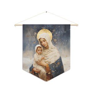 Pode incluir: Uma tapeçaria de parede com uma pintura em aquarela de uma mulher e uma criança. A mulher usa um véu branco e uma auréola dourada. A criança está com uma roupa branca. O fundo é uma cena azul e com neve.