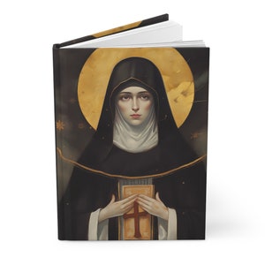 Puede incluir: Un diario negro y dorado con una pintura de una monja sosteniendo un libro. La monja lleva un hábito negro y un velo blanco. El fondo es azul oscuro con estrellas doradas.