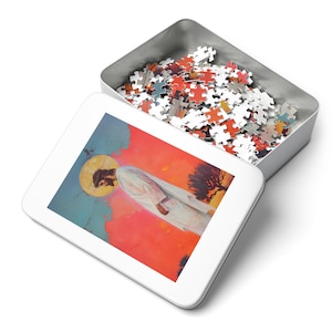 May include: A white metal tin box containing a colourful jigsaw puzzle. The puzzle depicts a painting of Jesus Christ standing in a desert landscape with a red and orange sky.