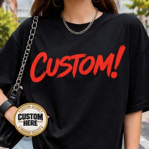 May include: Black t-shirt with the word "CUSTOM!" in red, brush-style lettering. A circular patch on the sleeve reads "CUSTOM HERE" with "CUSTOM DESIGN" and "PREMIUM QUALITY" text. A silver chain necklace and black purse are also visible.