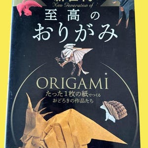 Puede incluir: Un libro titulado "Origami" con texto japonés e ilustraciones de animales de papel plegado. La portada presenta un dinosaurio marrón, un pájaro rosa y un erizo marrón. El título está en inglés y japonés.