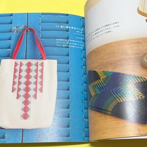 Puede incluir: Un bolso tote blanco con asas rojas y un patr&oacute;n geom&eacute;trico en rojo y azul claro. El bolso se muestra sobre un fondo azul, lo que sugiere un art&iacute;culo artesanal o hecho a mano.