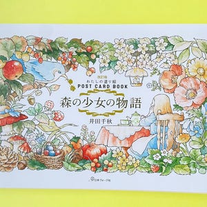 May include: A rectangular postcard book featuring a watercolour illustration of a forest scene with a person sitting at a table, surrounded by flowers, berries, mushrooms, and a blue bird. The text reads "POST CARD BOOK" and "森の少女の物語".
