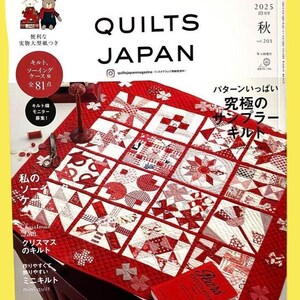 May include: The cover of "Quilts Japan" magazine displays a red and white patchwork quilt. The magazine cover has Japanese text and illustrations of bears and other items. A red book is on the table next to the quilt.
