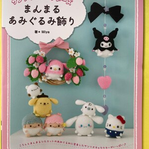 Puede incluir: Una portada de libro de manualidades titulada Sanrio Characters Manmaru Amigurumi Kazari de Miya, que muestra figuras de Sanrio tejidas a ganchillo, incluyendo a My Melody en una corona, Kuromi, Pompompurin, Little Twin Stars, Cinnamoroll y Hello Kitty.