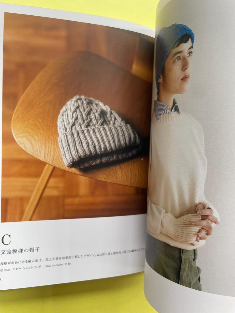 May include: A beige knit beanie with a textured cable pattern and a ribbed cuff. The page includes the text C, 交差模様の帽子, and How to make: P.36. The beanie is displayed on a wooden surface next to a photograph of a person wearing a blue beanie.