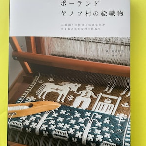 Peut inclure: Une couverture de livre montrant une photographie d'un métier à tisser en bois avec un textile brun foncé et blanc à motifs de chevaux et de personnages. Le texte japonais indique : ポーランド ヤノフ村の絵織物, 二重織りの技法と伝統文化が生まれた小さな村を訪ねて, 織り 秋元尚子, 文 藤田泉, 誠文堂新光社.