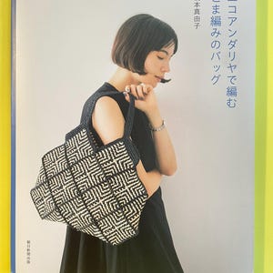 May include: A craft book cover featuring a black and white geometric patterned crochet bag. The Japanese text on the cover reads: エコアンダリヤで編むこま編みのバッグ, 橋本真由子, 朝日新聞出版. The design showcases a structured tote with a repeating square motif.