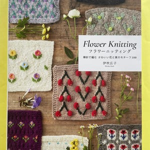 Könnte beinhalten: Ein Buch mit dem Titel "Flower Knitting" mit japanischem Text, das verschiedene gestrickte Blumen- und Fruchtmotive zeigt. Das Cover zeigt mehrere gestrickte Quadrate mit floralen Designs in Farben wie Rosa, Lila und Grün, vor einem Holzgrund.
