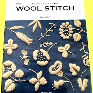 May include: A book titled "WOOL STITCH" with Japanese text, featuring embroidered floral designs in cream thread on a dark blue background. The cover showcases various stitched flowers, leaves, and a butterfly.