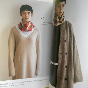 May include: A knitted neck warmer featuring a multi-coloured argyle pattern in shades of red, yellow, white, and grey. The neck warmer is displayed on a person wearing a beige V-neck sweater and also on a person wearing a brown coat.