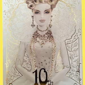 May include: A magazine cover with the text "Dollybird" in gold lettering. The cover features a doll with elaborate makeup, jewelry, and a white gown. The number "10th" is prominently displayed in gold.