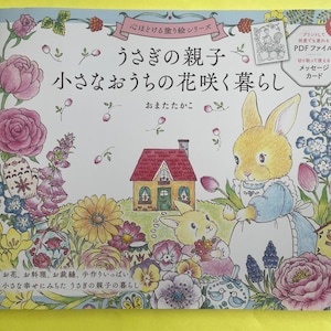 May include: A coloring book titled "うさぎの親子 小さなおうちの花咲く暮らし" featuring a light-colored cover with illustrations of two rabbits, a small house, and various colorful flowers including pink roses, yellow daisies, and blue blossoms.