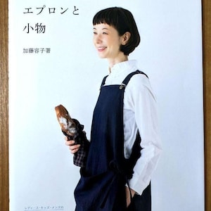 Könnte beinhalten: Ein Buchcover mit japanischem Text, das eine Frau in einer dunkelblauen Schürze und einem weißen Hemd zeigt, die Brot hält. Das Buch trägt den Titel "Schürzen und Accessoires". Das Cover enthält auch japanischen Text und die Worte "36 Punkte".