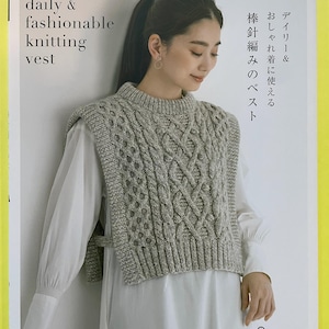 May include: A softcover book titled daily & fashionable knitting vest by applemints featuring a grey cable-knit vest with a mock neck and side ties worn over a white long-sleeved shirt. The cover includes Japanese text and a logo.
