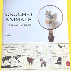以下が含まれることがあります： 「CROCHET ANIMALS」というタイトルの本。日本語のテキストがあり、拡大鏡で拡大されたかぎ針編みのリスが特徴です。表紙には世界地図とかぎ針編みの動物のパターンも表示されています。