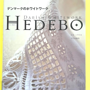 Op de afbeelding: Een boekcover met de titel "Danish Whitework HEDEB0" in grote letters. De cover toont een close-up van witte kanten borduursels. Japanse tekst is ook zichtbaar.