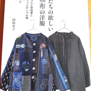 May include: A book cover featuring two jackets and Japanese text. The jacket on the left is a patchwork design in shades of blue, with circular and geometric patterns. The jacket on the right is a solid dark gray color. The book title is in Japanese.