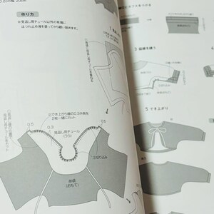 Op de afbeelding: Een open boek met gedetailleerde naaipatroondia's. De diagrammen bevatten afmetingen in centimeters en Japanse tekst, die de stappen voor de kledingconstructie illustreren. De pagina's zijn wit met zwarte en grijze illustraties.