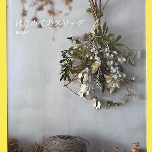 May include: A book cover with Japanese text and a floral arrangement. The arrangement includes dried flowers, green leaves, and small blue berries. A spool of twine and dried plants are at the bottom of the image.