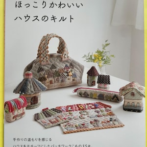 以下が含まれることがあります： 「ハウスのキルト」というタイトルの日本語の本。キルトのハンドバッグ、家型のアイテム、ペンケースが特徴です。アイテムはパッチワークのデザインで装飾されています。本には「LABORIS」という言葉が入ったパッチワークキルトも掲載されています。