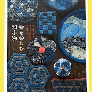 以下が含まれることがあります： 木製の表面に配置された、藍色のキルトアイテムの詰め合わせ。コースター、プレースマット、小さなポーチなど。さまざまな幾何学模様と花柄が特徴です。日本語のテキストが表示されています。