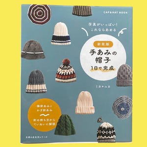 以下が含まれることがあります： 様々なスタイルと色のニットと編み物の帽子が特徴の書籍の表紙。表紙には日本語のテキストとイラストが含まれており、背景はティール色、縁は黄色です。書籍のタイトルは「CAP & HAT BOOK」です。