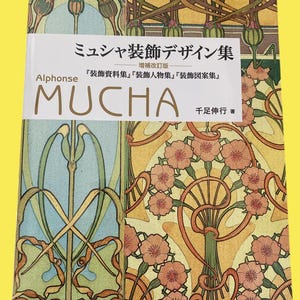 Op de afbeelding: Boekomslag met de Japanse titel "Mucha Decorative Design Collection", met de naam "MUCHA" prominent. De omslag toont Art Nouveau bloemen- en geometrische patronen in oranje, groen en bruin. Het boek is een designcollectie.