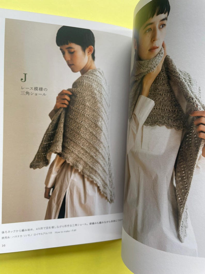 May include: A beige triangular crochet shawl featuring a delicate lace pattern with a scalloped edge. The shawl is displayed in a book, shown draped over the shoulders and wrapped around the neck, showcasing the textured yarn and openwork design.