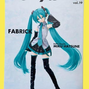 May include: A magazine cover featuring a doll with long, turquoise pigtails and a matching outfit. The magazine title "Dollybird" is at the top, with "vol.19" below it. The text "FABRICK" and "MIKU HATSUNE" are also visible.