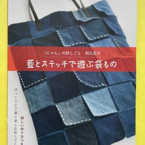 Op de afbeelding: Een knutselboekcover met een patchwork draagtas gemaakt van verschillende tinten blauwe denimstof met witte decoratieve stiksels. De Japanse tekst bevat de titel 藍とステッチで遊ぶ袋もの, de auteursnaam 和久亞子 en de serienaam レディブティックシリーズ.