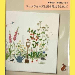 May include: A book cover with an embroidered garden scene, including flowers, a bird, a watering can, and a shovel. The title is in Japanese. The book is about the Cotswolds and Lake District.